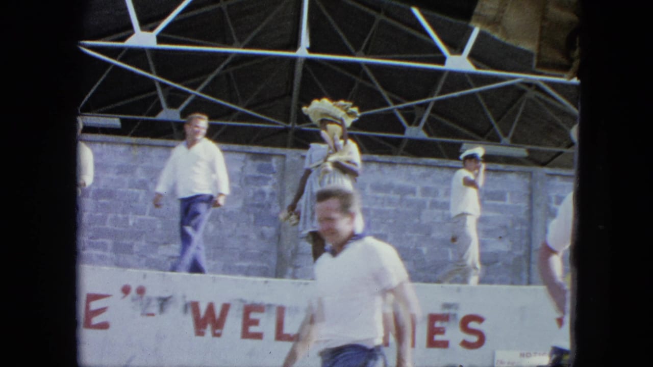 Adults on a stage near a partial WELCOME sign under a metal truss roof.
