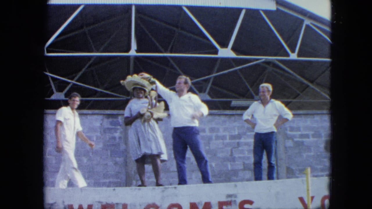 Four adults are visible on a stage as one man raises his arm beside a woman in a hat.