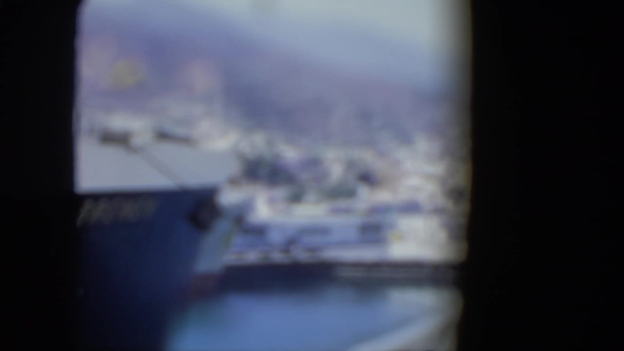 Soft 8mm frame from the Venezuela port clip, showing a blurred harbor view through dark gate edges with water and ship forms visible.