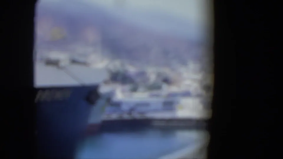 Soft 8mm frame from the Venezuela port clip, showing a blurred harbor view through dark gate edges with water and ship forms visible.