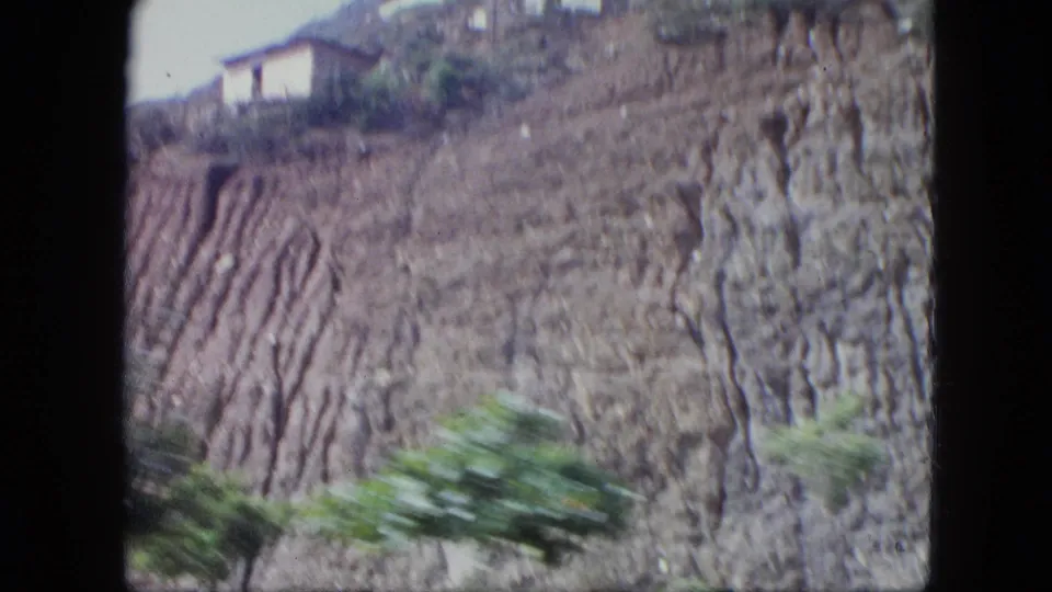 A soft, handheld 8mm frame shows striated cliff or hillside soil with blurred greenery passing in front.