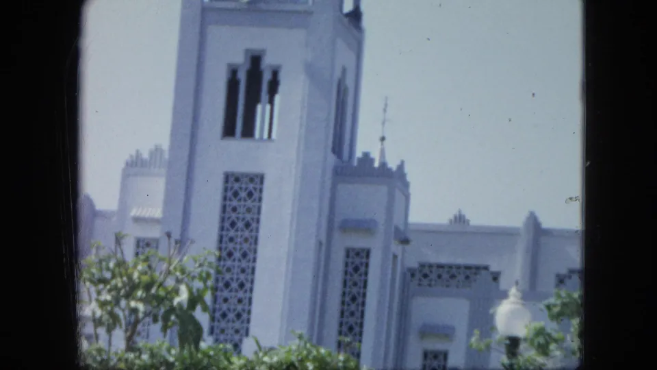 1964 Venezuela 8mm frame with the white tower, patterned vertical panels, trees, and a round garden lamp.