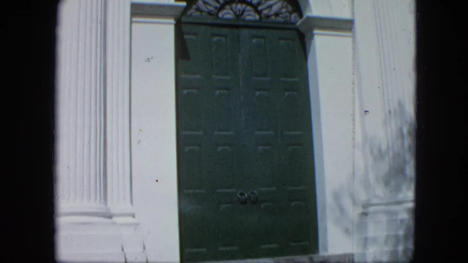 Close 8mm view of tall green paneled double doors set between white columns on a formal building facade in Venezuela.