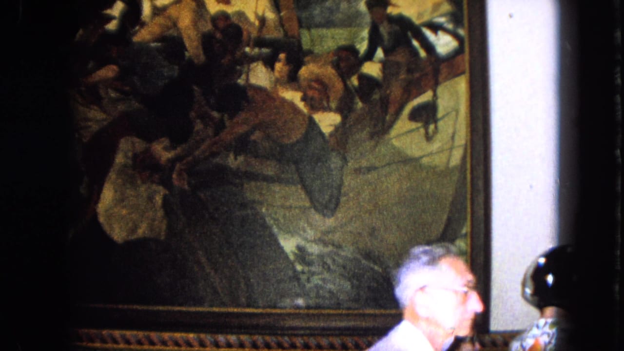 Visitor in glasses passes in front of a large framed painting indoors.