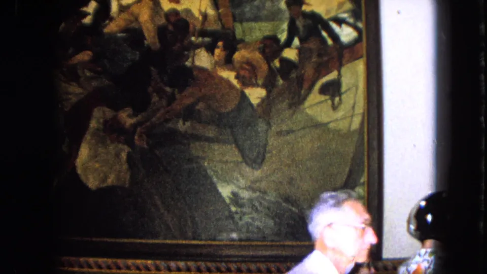 A man in glasses is visible near a large historical painting during 1964 Venezuela home-movie travel footage.