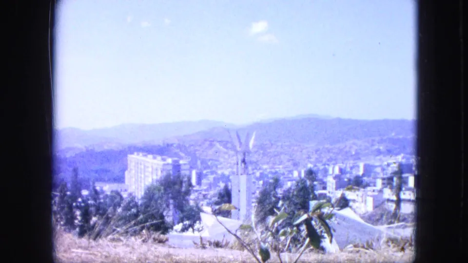 1964 Venezuela footage shows a hazy city panorama set below mountains, with buildings, vegetation, and a tall monument-like form.