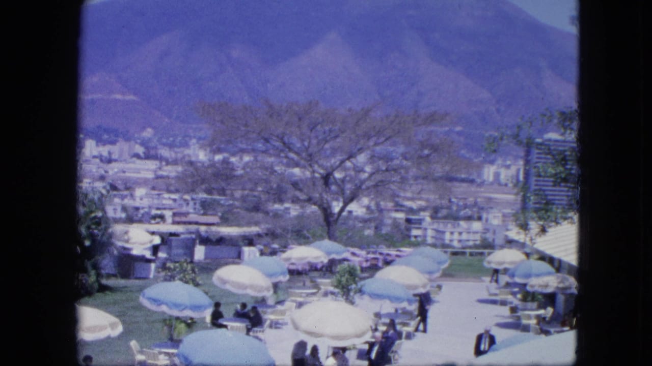 Terrace social gathering with umbrellas, guests, city buildings, trees, and mountains beyond.