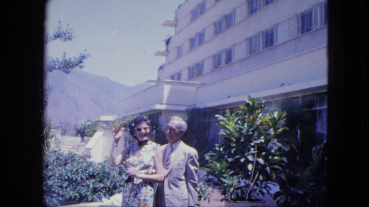 Couple posing outside a hotel terrace with plants and mountains behind them.