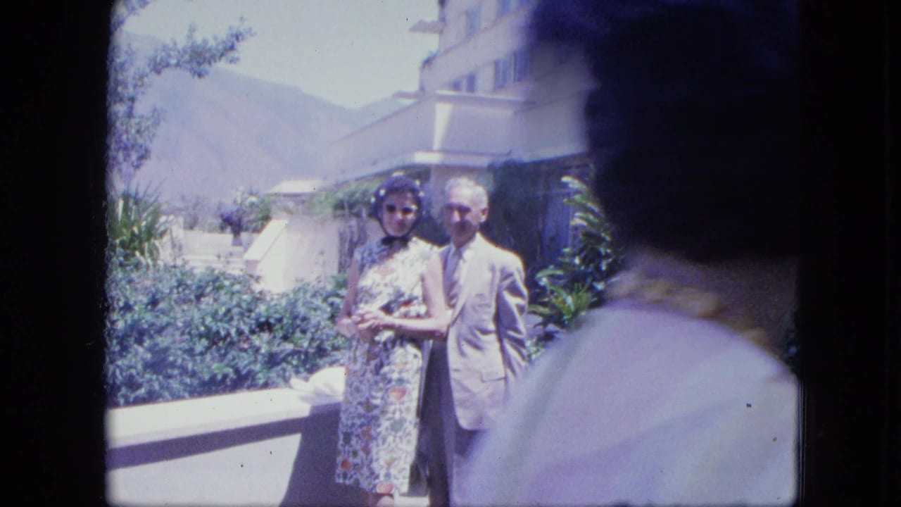 Elderly couple posing outside a modern hotel with mountains behind them.
