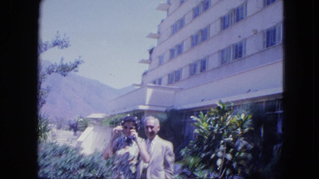 Couple standing near hotel landscaping, with the building and mountains visible.