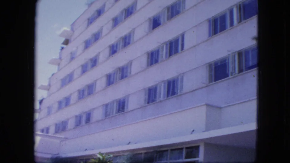 1964 Venezuela home-movie frame focused on the hotel exterior, showing rows of windows, a projecting entrance area, and bright daylight.