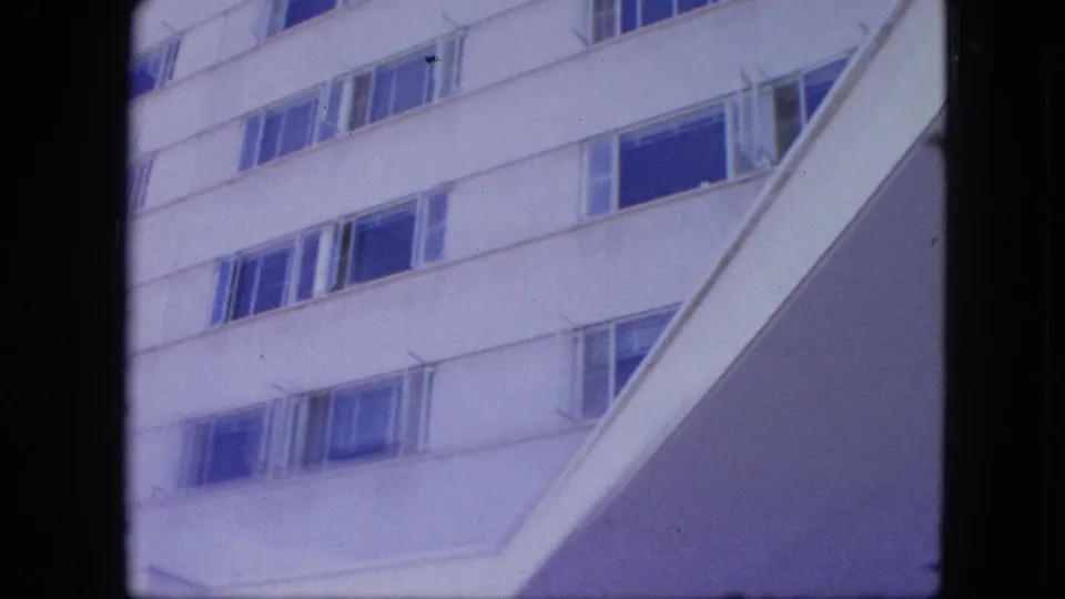 Low-angle 8mm view of a white high-rise with window rows and a strong angled architectural edge crossing the frame.