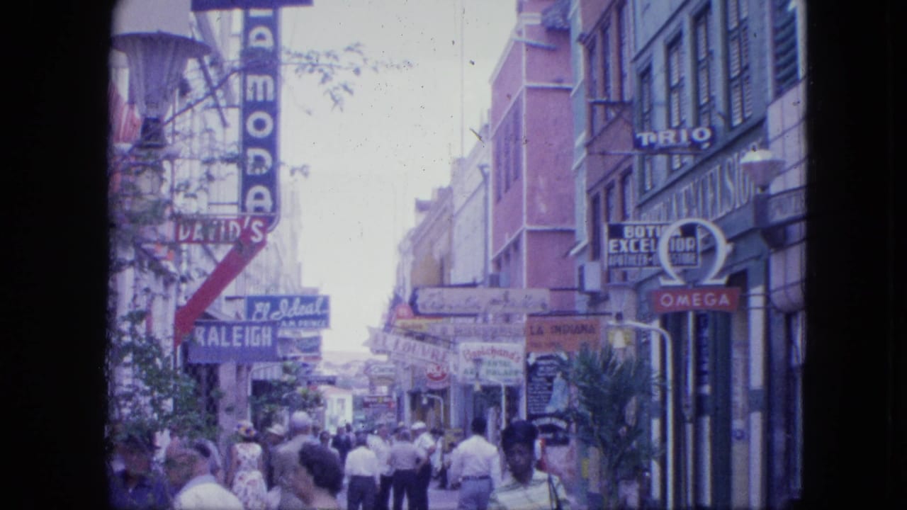 Busy sidewalk with pedestrians passing storefronts and vintage shop signs.