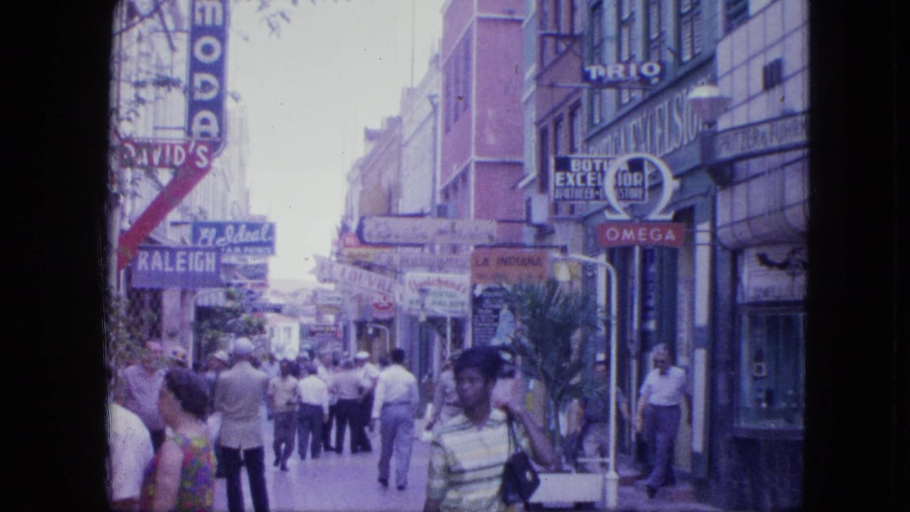 1964 Venezuela street scene showing pedestrians moving past shopfronts with David's, Omega, and other visible signage.