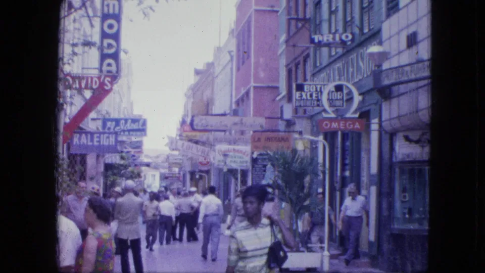 1964 Venezuela street scene showing pedestrians moving past shopfronts with David's, Omega, and other visible signage.
