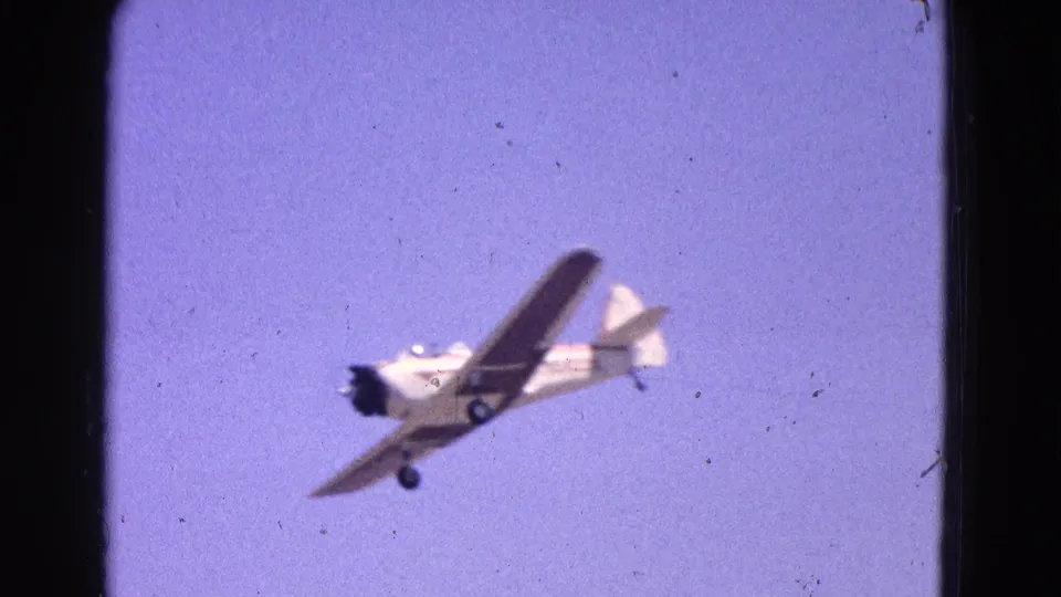 Small propeller plane seen overhead in 1964 Washington, DC area 8mm footage, with landing gear and wing markings visible.