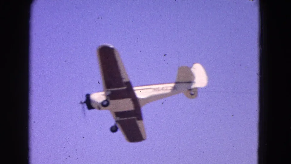 The airplane appears banked in a 1964 home-movie frame, showing its wing, fuselage, tail, and fixed landing gear.
