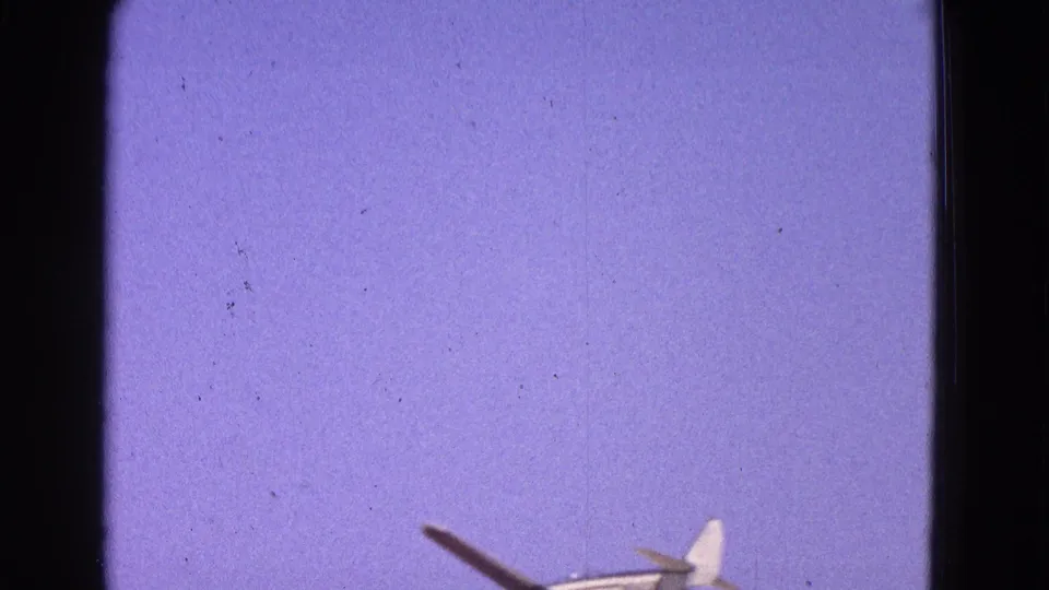 The airplane moves partly out of frame near the bottom of the 1964 8mm shot, leaving mostly pale blue sky and film texture visible.