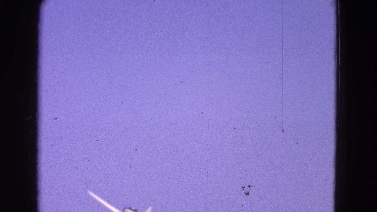 Small white airplane appears low in the frame against a purple-blue 8mm sky with visible film dust and scratches.