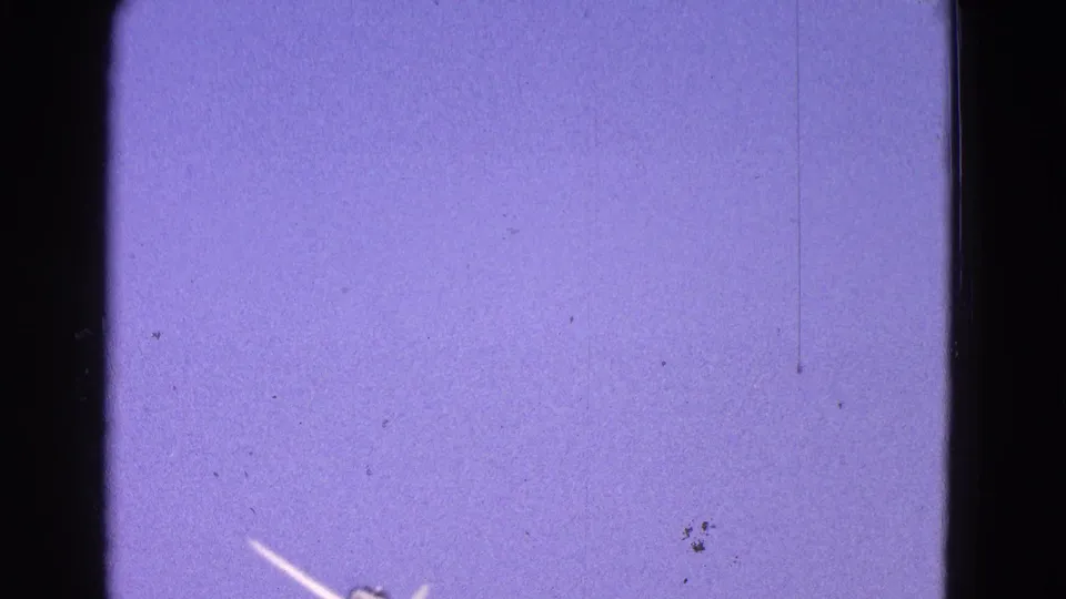 Small white airplane appears low in the frame against a purple-blue 8mm sky with visible film dust and scratches.