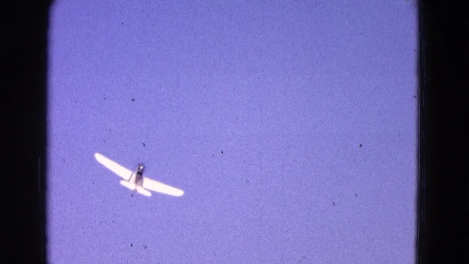 Small white airplane banks overhead against a purple-blue sky in 8mm home-movie footage from Washington DC in 1964.