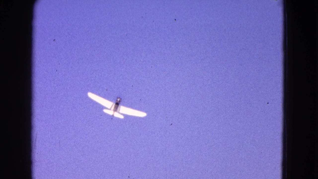 Small white plane flying in a blue sky with dark 8mm film borders.