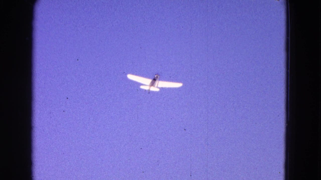 White plane higher in the blue sky within an 8mm film frame.