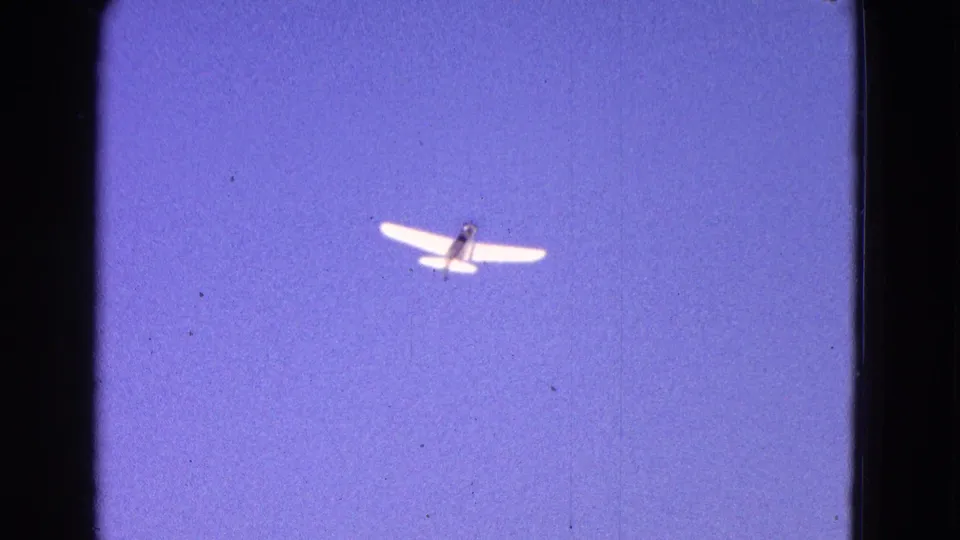 Small white aircraft in flight against blue sky, framed by dark 8mm gate edges in Washington, DC area footage from 1964.