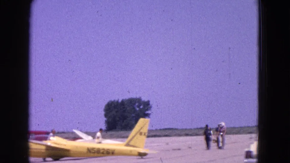 Yellow aircraft marked N5828V sits on a sunlit airfield tarmac with several distant people nearby in 1964 Washington, DC area footage.