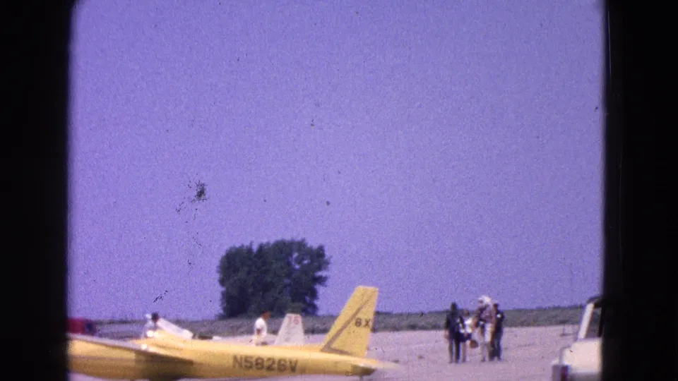 A yellow aircraft with visible registration N5828V is parked on an airfield, with distant people and equipment at the edge of the frame.