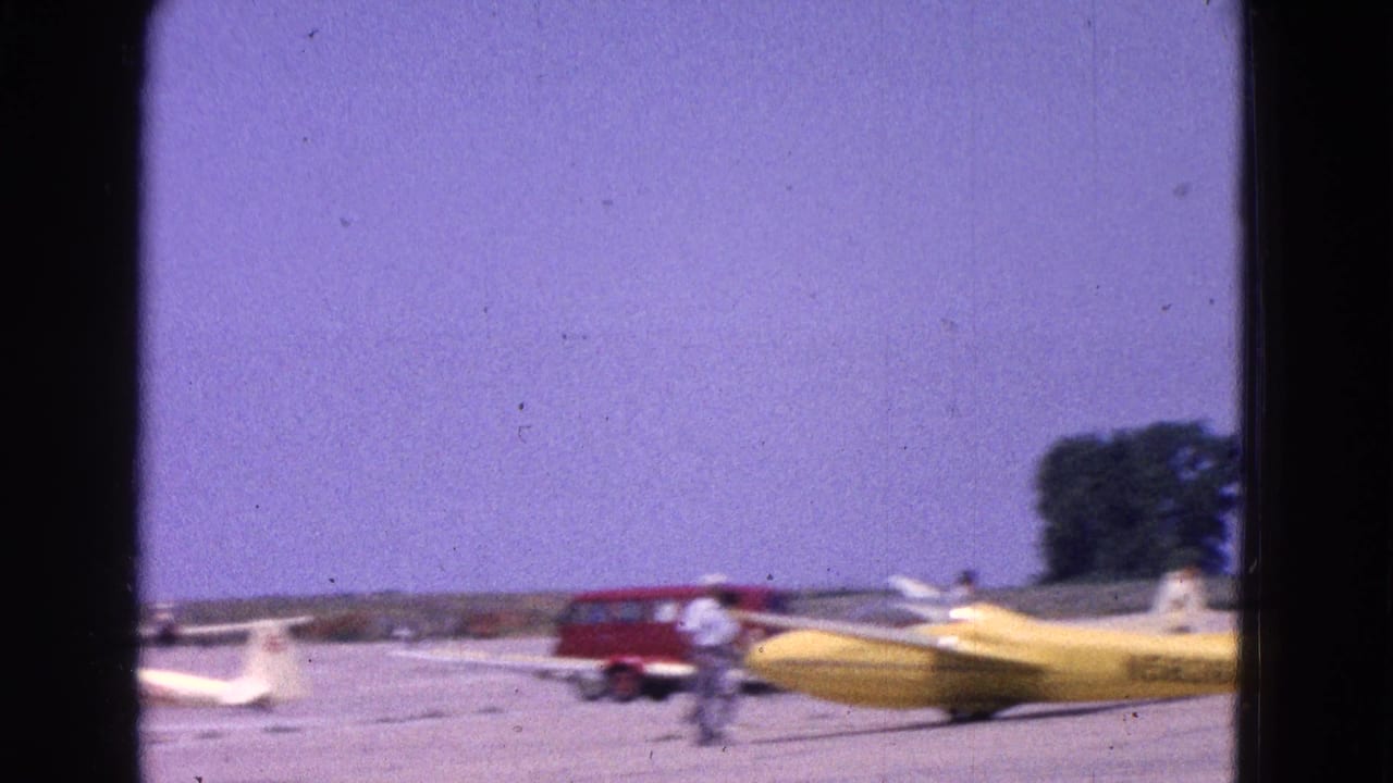 1964 Washington, DC home-movie frame showing small aircraft on a tarmac, including a yellow plane, with a red van and people in the background.