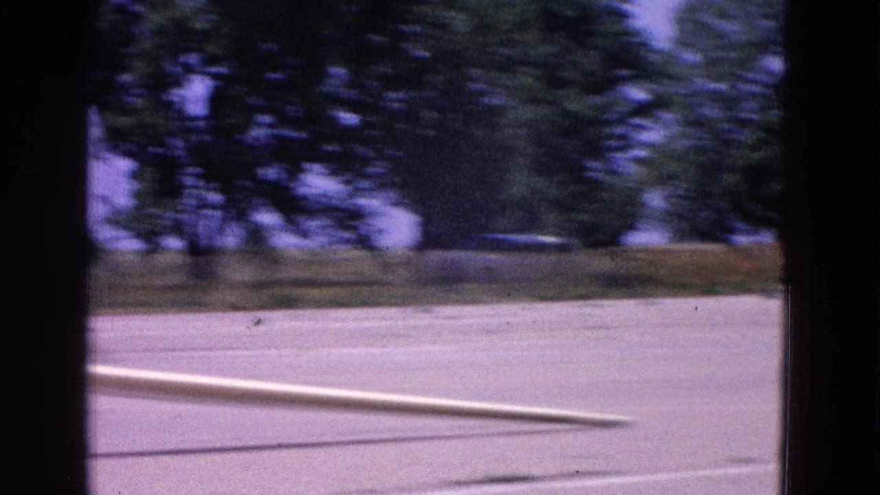 Runway view with blurred trees, tarmac, and the edge of an aircraft entering frame.