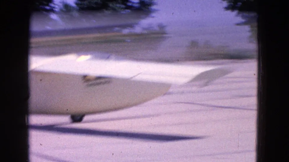Close 1964 8mm view of a white glider passing across the Washington, DC runway, with fuselage, wing, and wheel visible.