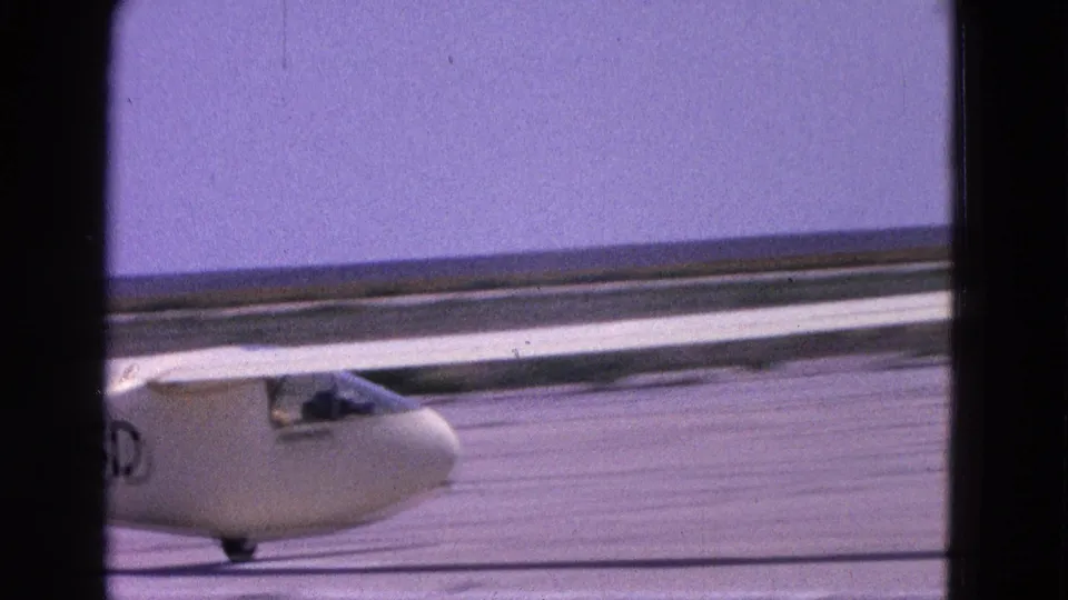 1964 Washington, DC 8mm frame showing the nose and wing of a white glider taxiing across a bright runway.