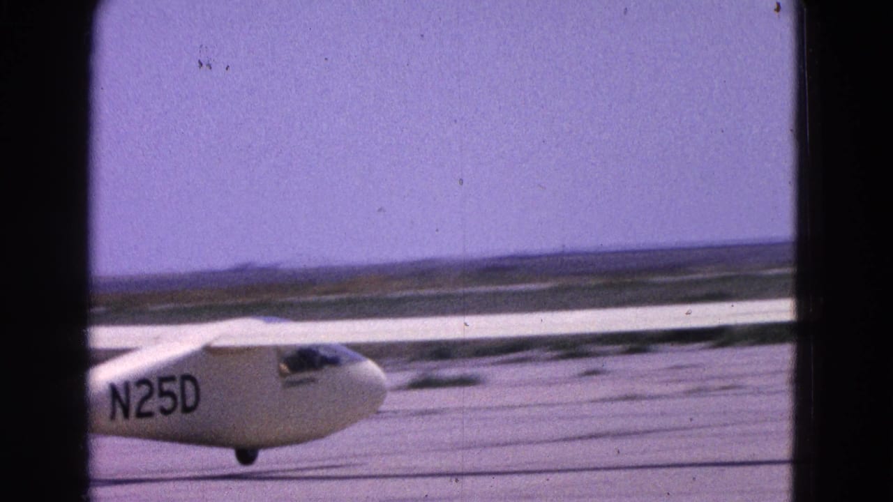 White glider marked N25D partly crossing a runway under a blue sky.