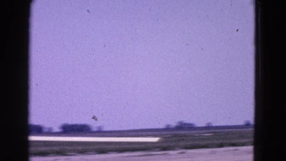 The 8mm frame holds on runway pavement, low landscape, and blue sky after the glider has largely passed from view.