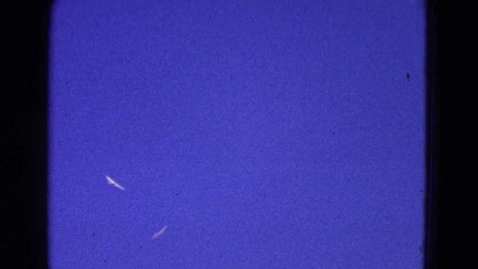 1964 Washington, DC home-movie frame with the aircraft reduced to bright marks against a deep blue sky.