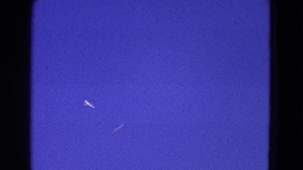 1964 Washington, DC home-movie frame showing blue sky, small distant aircraft shapes, and visible 8mm film gate edges.