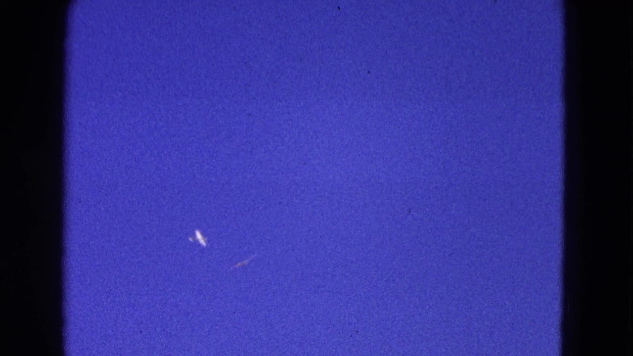 1964 Washington, DC frame with distant light aircraft shapes against blue sky and visible 8mm texture.