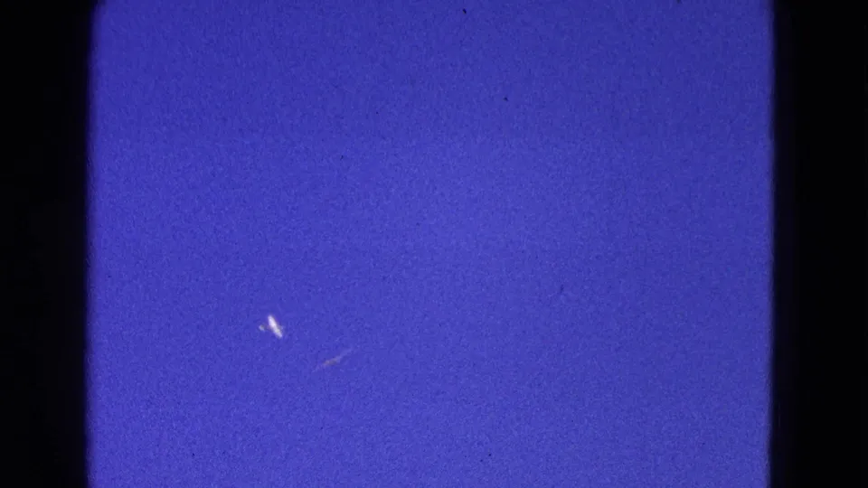 1964 Washington, DC frame with distant light aircraft shapes against blue sky and visible 8mm texture.