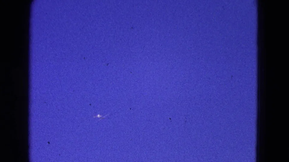 Home-movie frame from the 1964 Washington, DC clip showing blue sky, a tiny bright aircraft mark, and 8mm grain.