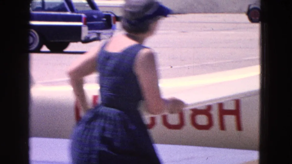 1964 Washington DC home-movie frame showing a woman near the aircraft wing with partial red registration markings on the fuselage.