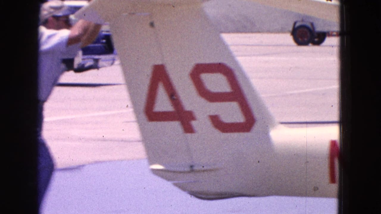 Man beside a small white airplane tail marked with red number 49 on an airfield.