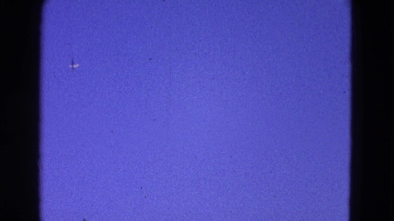 Blue sky seen through dark film frame borders with a tiny distant aircraft shape.