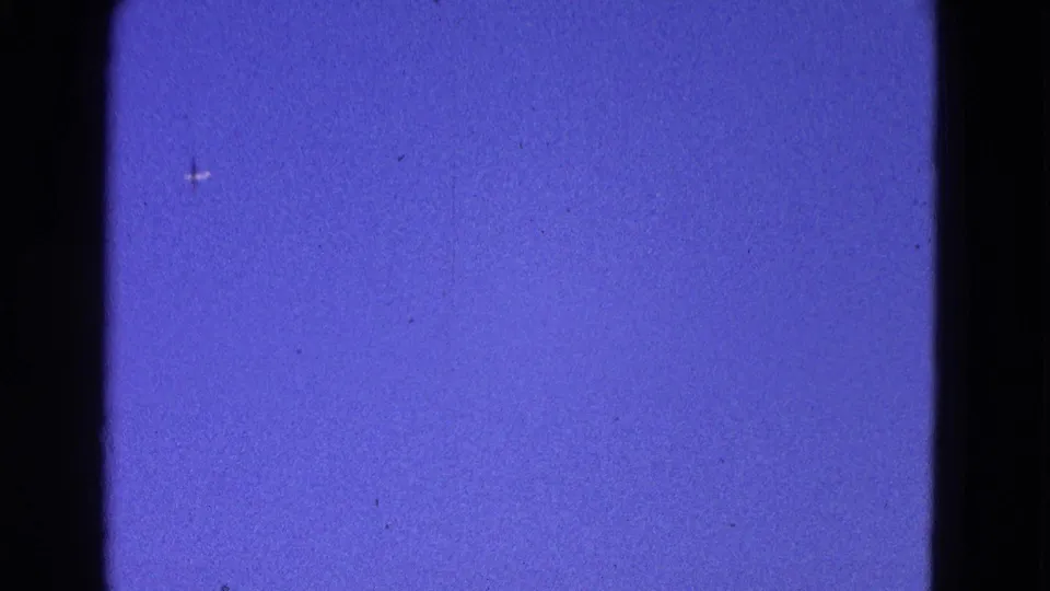 Blue sky from the Washington DC aviation footage, framed by dark 8mm gate edges with a small distant aircraft shape.
