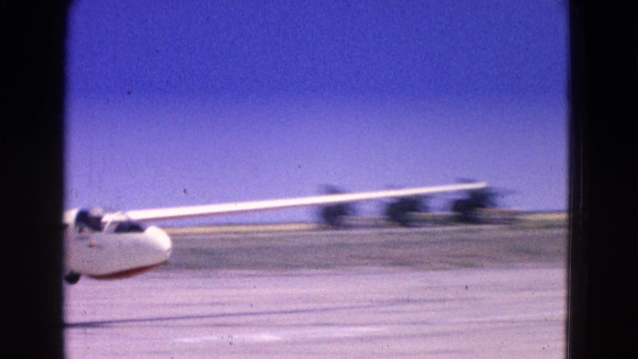 White glider moving along a runway under a blue sky, partly blurred by motion.