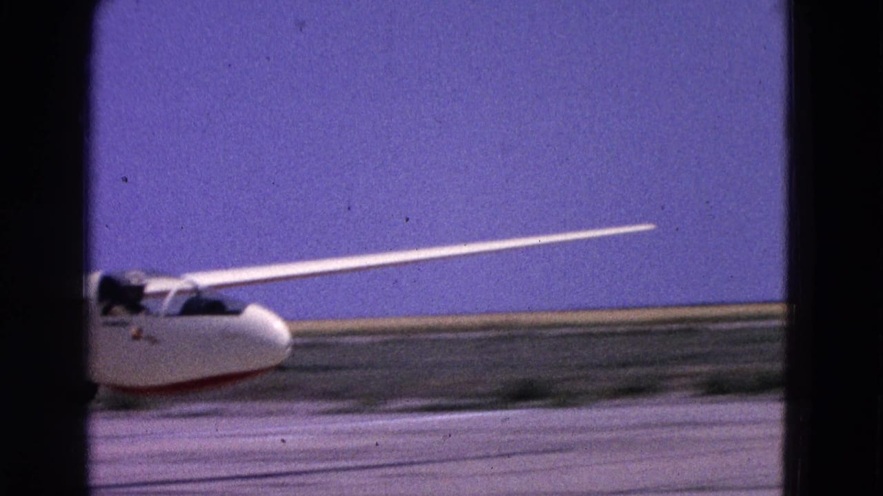 White glider on a runway in the supplied 1964 Washington, DC footage, with a cockpit occupant or pilot visible as it picks up speed.