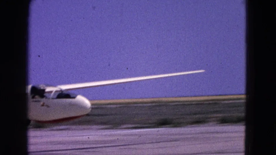 White glider on a runway in the supplied 1964 Washington, DC footage, with a cockpit occupant or pilot visible as it picks up speed.