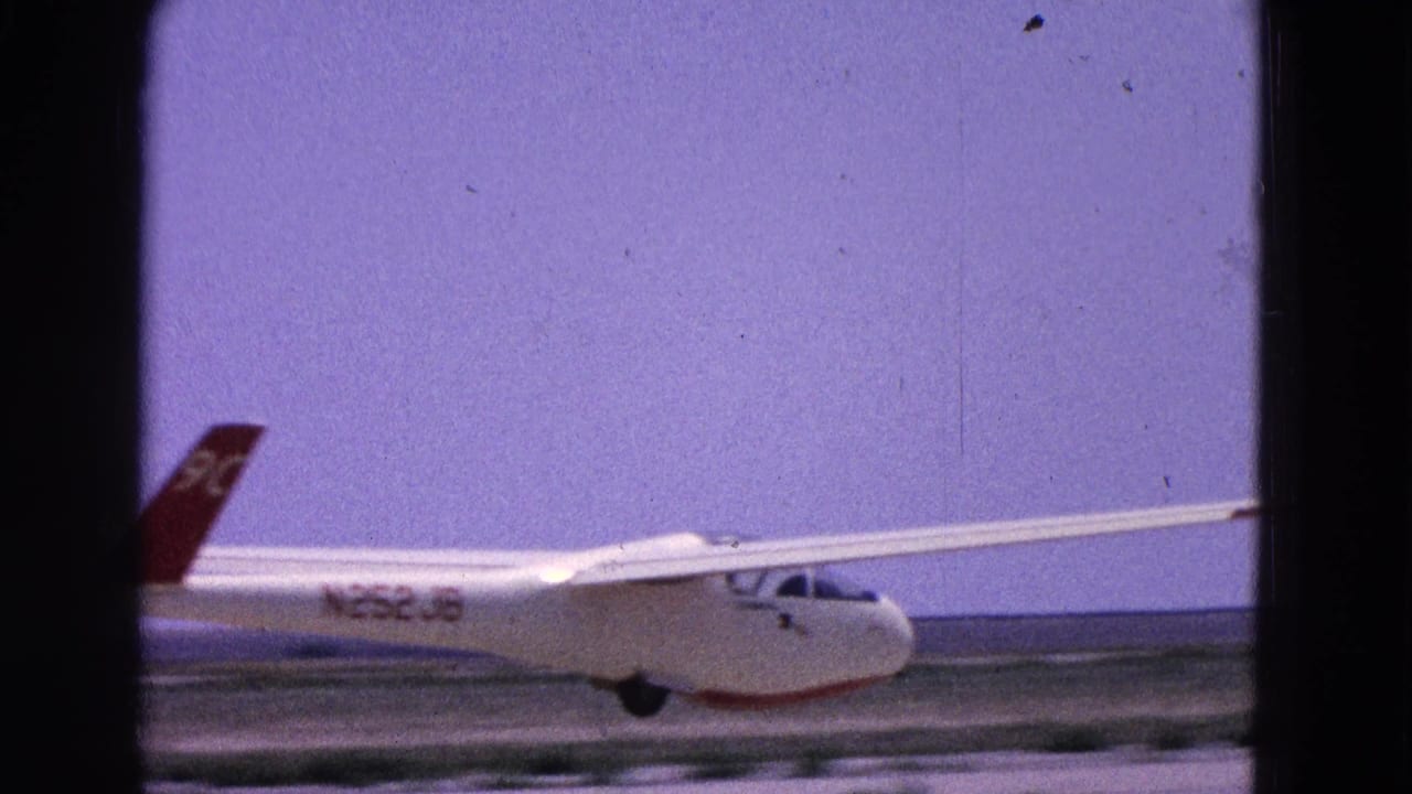 The glider continues down the runway, with red tail markings and a low airfield horizon visible.