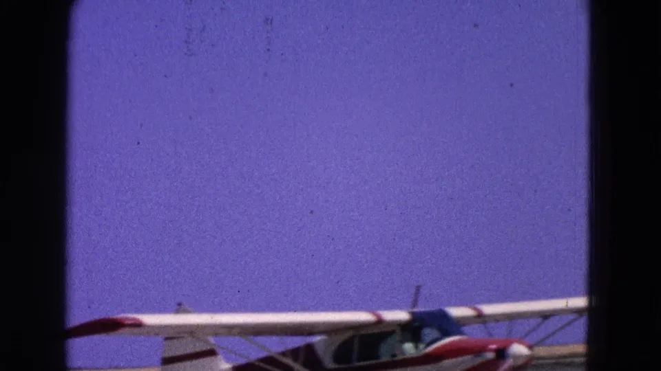 1964 Washington, DC 8mm frame showing a small white-and-red aircraft low in the frame near a runway under a clear blue sky.